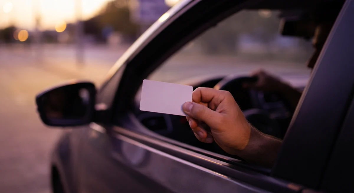 A driver's hand passing a licence card through a car window to an unseen officer, softly lit in warm gold tones
