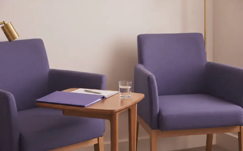 A quiet consultation room with a folder, notepad and two chairs, in restrained purple and gold tones.