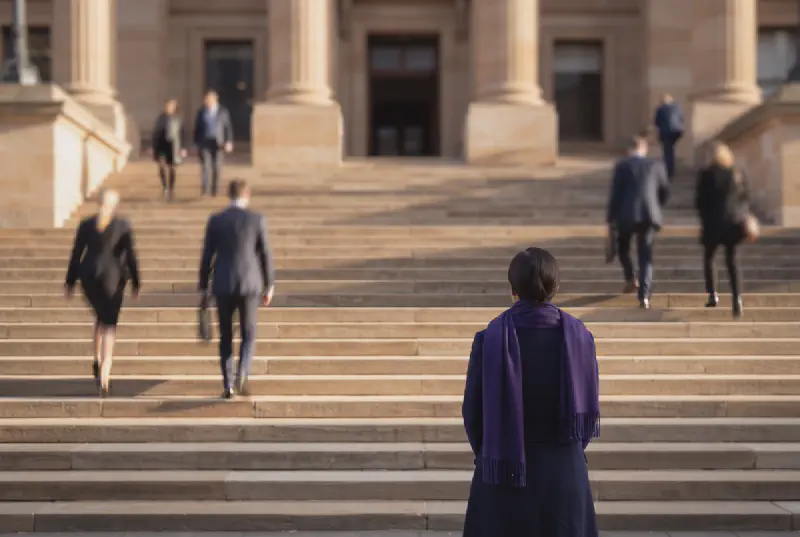 Sandstone courthouse steps with blurred figures in gold morning light and a person in a royal purple scarf in the foreground